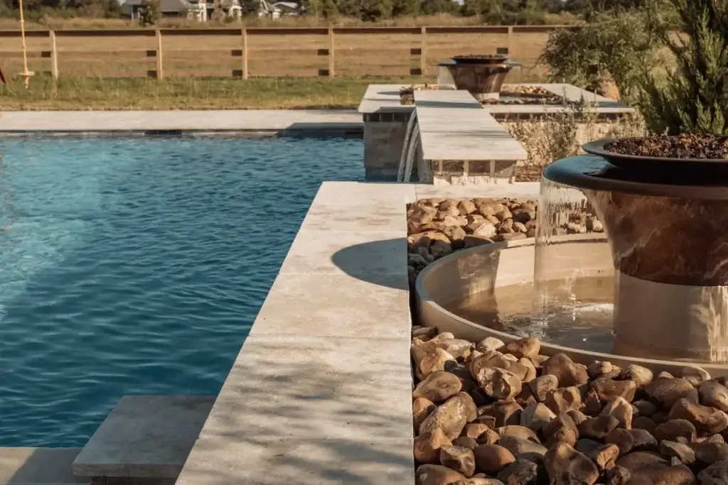 Backyard pool with stone water feature and fire pit, wooden fence in background.